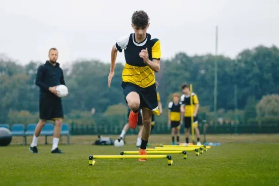 Young male football players running through speed hurdles on grass