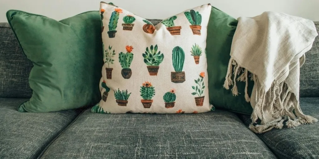 A sage green couch with throw pillows and throw blanket