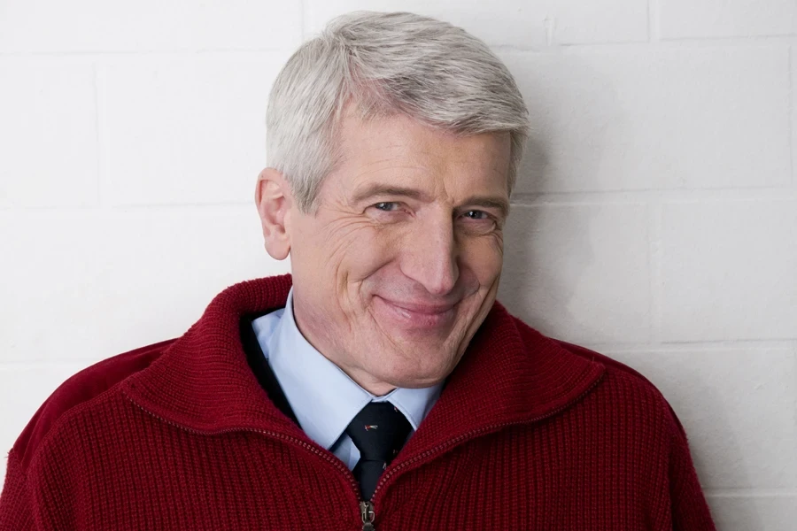 An elderly man in a red quarter-zip sweatshirt