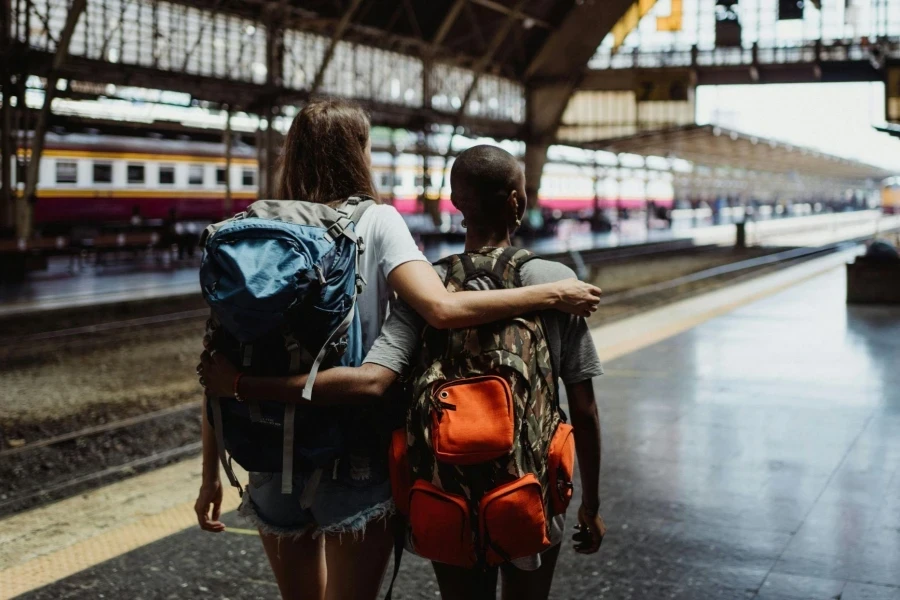 Back View of Two Women Walking with Backpacks at a Train Station