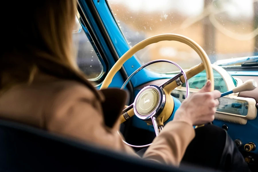 Back view of crop anonymous woman sitting on driver seat and driving retro car in daytime