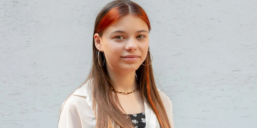 Beautiful teenage girl 13 years old with orange hair smiling against a white wall background