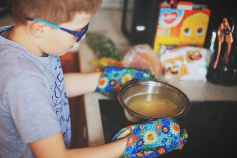 Boy in Glasses and Oven Gloves Carrying a Bowl of Soup