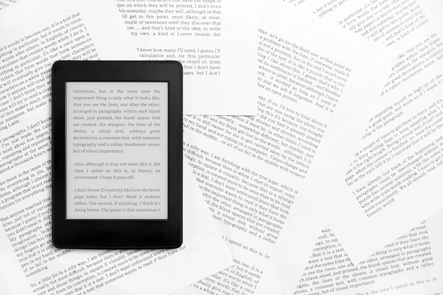 Electronic reader with the screen on and text on it, on paper sheets