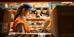 Female warehouse worker working on laptop at storage compartment