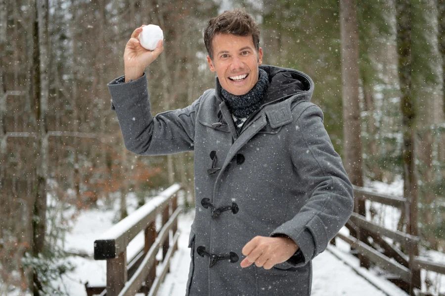 Man in a gray duffle coat throwing a snowball