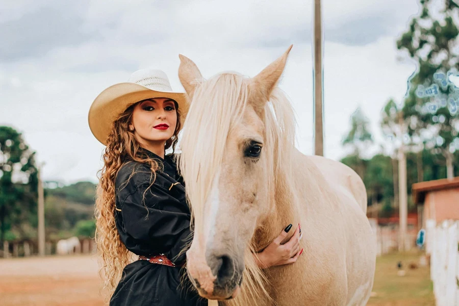 Stylish young lady embracing horse in paddock