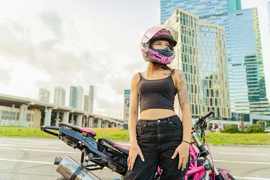 Woman in Black Spaghetti Strap Crop Top Standing Beside a Pink Motorcycle Wearing Safety Helmet