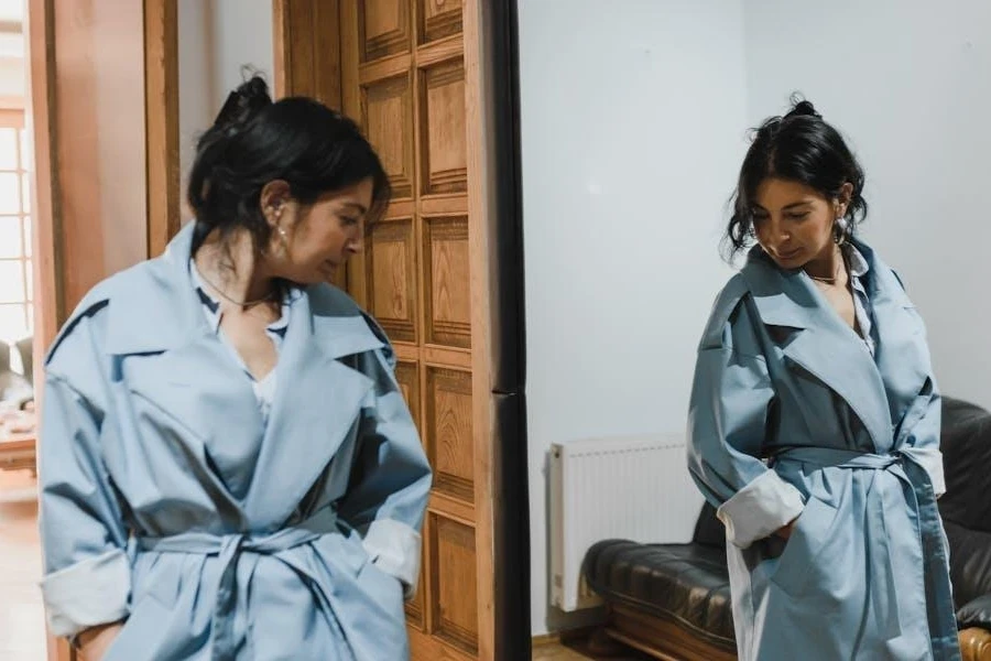 Woman in a blue belted coat in front of a mirror