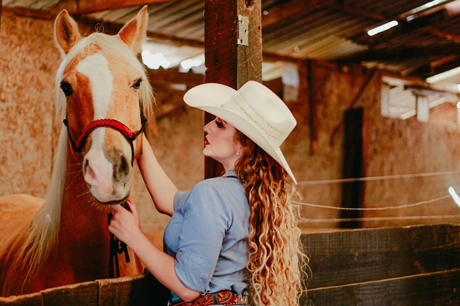 Young cowgirl stroking chestnut horse in paddock