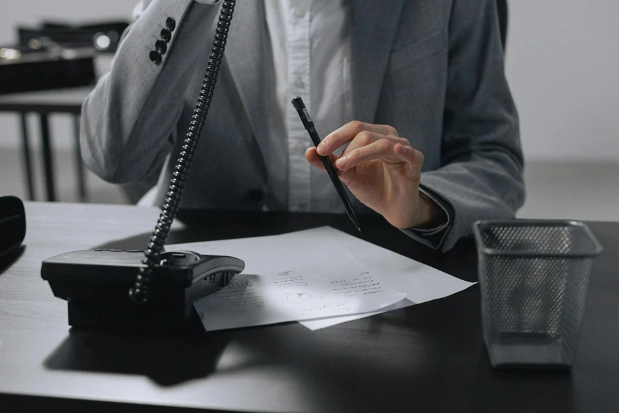 a man talking on wired telephone while holding pen