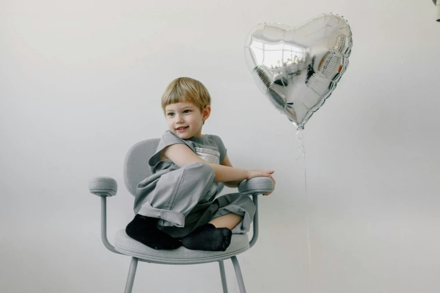 A Kid Sitting on a Chair Near a Silver Balloon