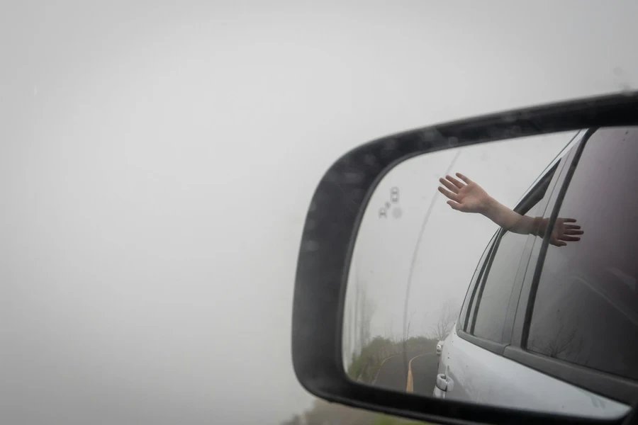 A Side View Mirror with a Reflection of a Person's Hand Sticking out from a Cars Window