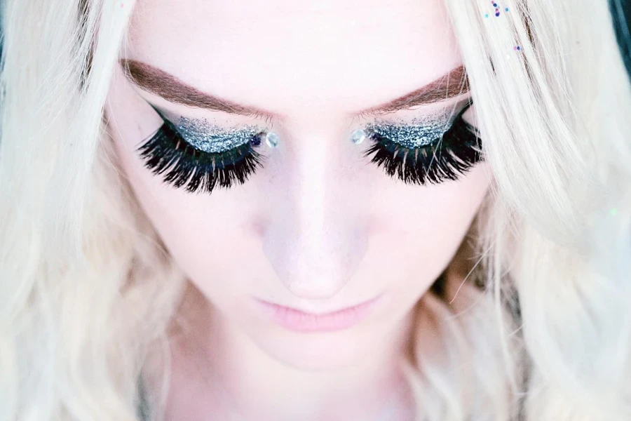 A close up portrait looking down on an 18 year old person wearing false eyelashes and glitter eye shadow