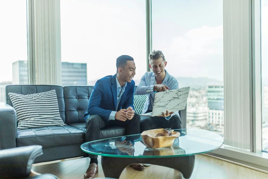 A couple of men sitting on a couch looking at a tablet