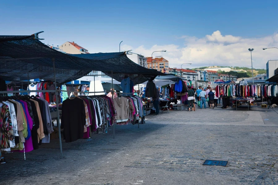 A large outdoor market is set up in a European city with many stalls selling clothing items.