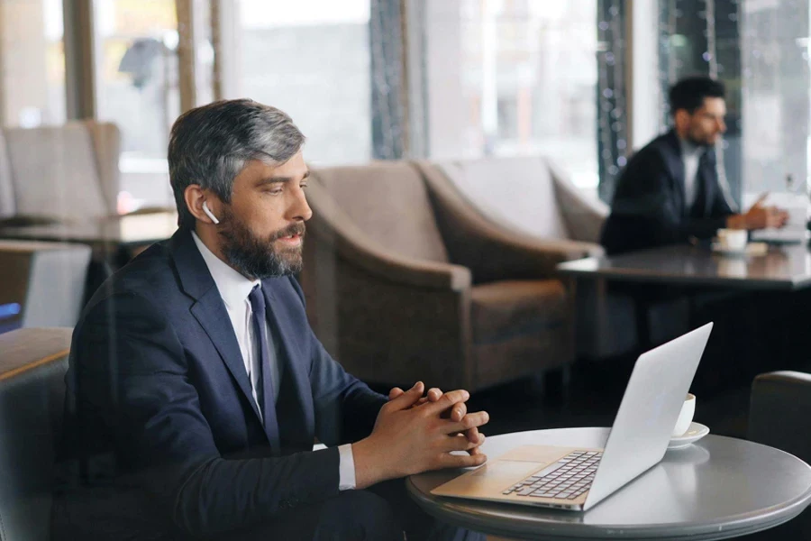 A man in business attire sitting at a table with laptops