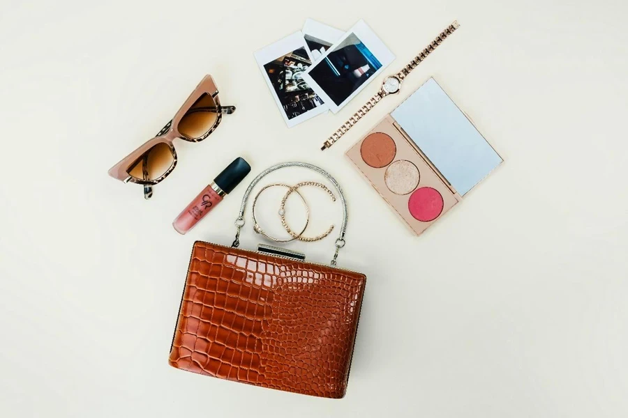 A purse, sunglasses, lipstick, and other items are laid out on a table