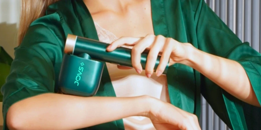 A woman in silk pajamas uses the JOVS Venus Pro II Hair Removal Device on her right arm