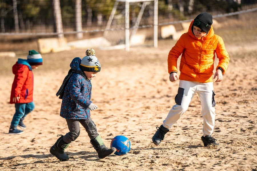 Boy in Orange Jacket and White Pants Playing a Ball