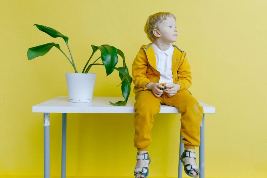 Boy in Yellow Jacket and Yellow Pants Sitting on White Table