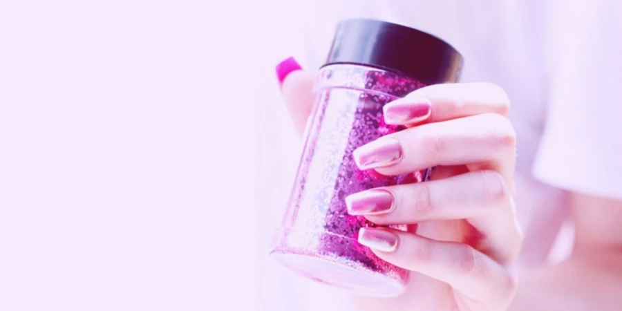 Close up of shiny hot pink acrylic nails and a bottle of magenta glitter