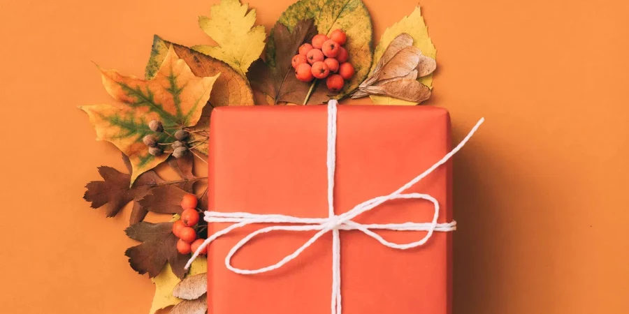 Gift box with minimal autumn leaves decor on orange background