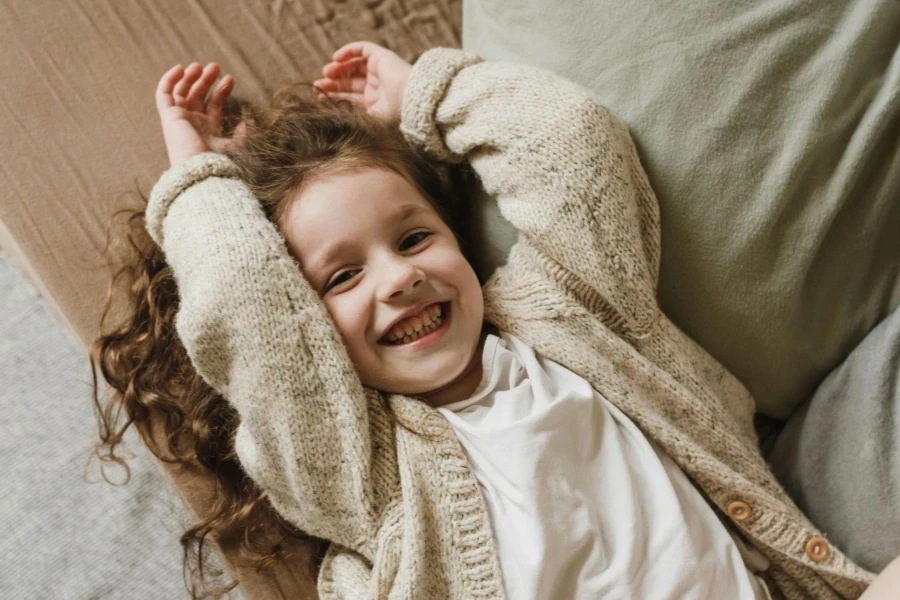 Girl in white long-sleeved sweater lying on bed