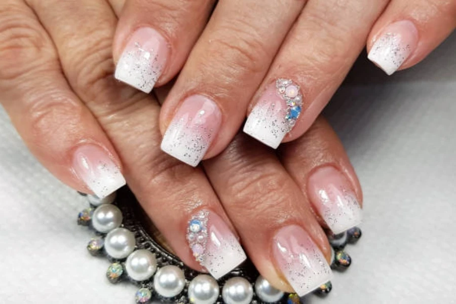 Glitter ombre white nails with small pearl accents on corners