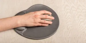 Hand on computer mouse on ergonomic gel pad with wrist support, rest on work desk