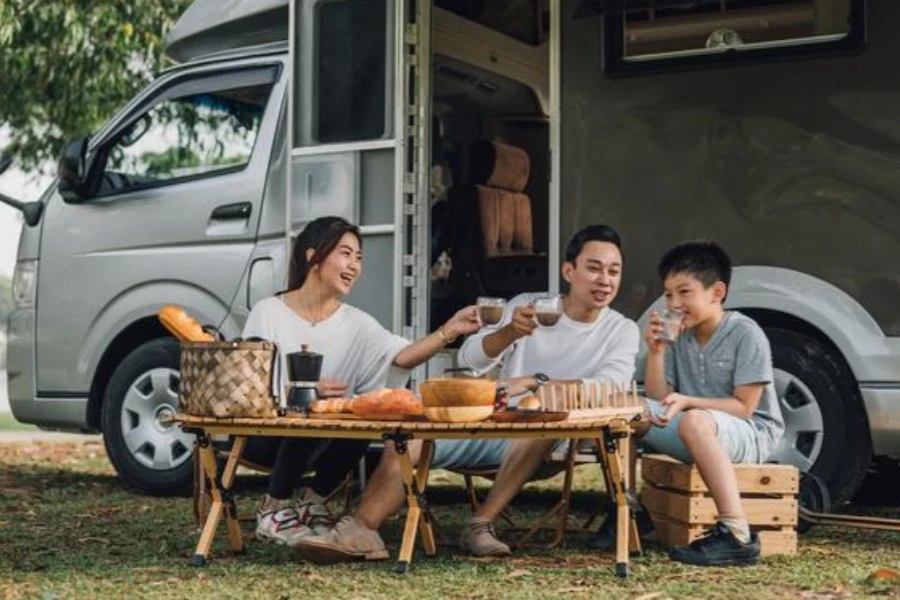 Happy Asian family talking at picnic table by their camper trailer in nature