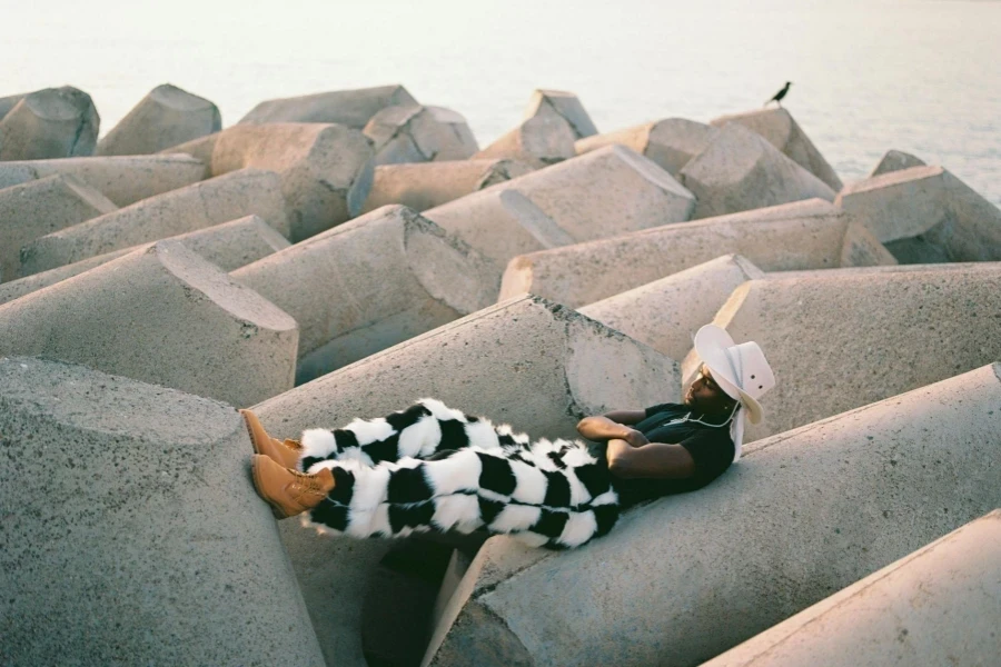 Man in Hat and Checkered Trousers Lying Down on Concrete Blocks