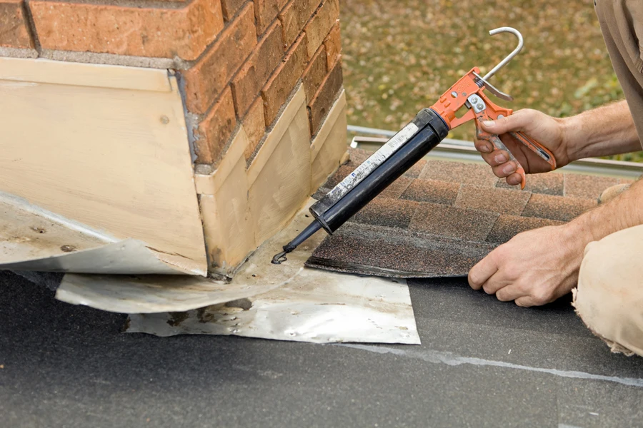 Roofer applying caulk to house chimney flashing