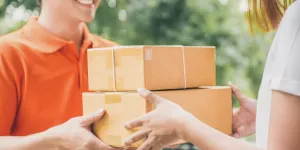 Smiling delivery man in orange uniform delivering parcel box to a woman customer