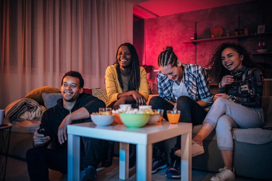 Students seated on sofa with cushions and blankets watching TV