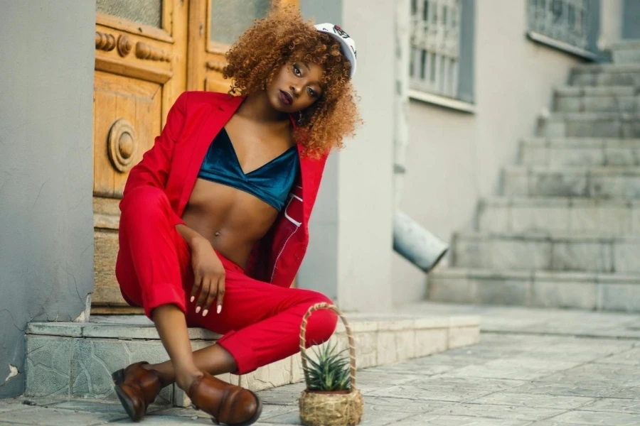 Woman Wearing Red Coat and Pants Sitting Outside Gray Building