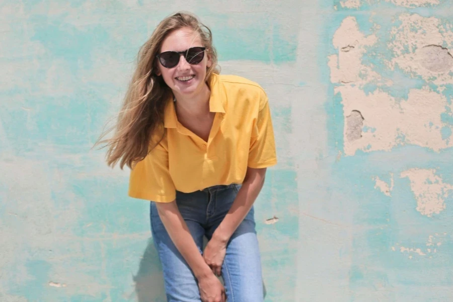 Woman Wearing Yellow Polo Shirt Standing in Front of Teal Concrete Wall