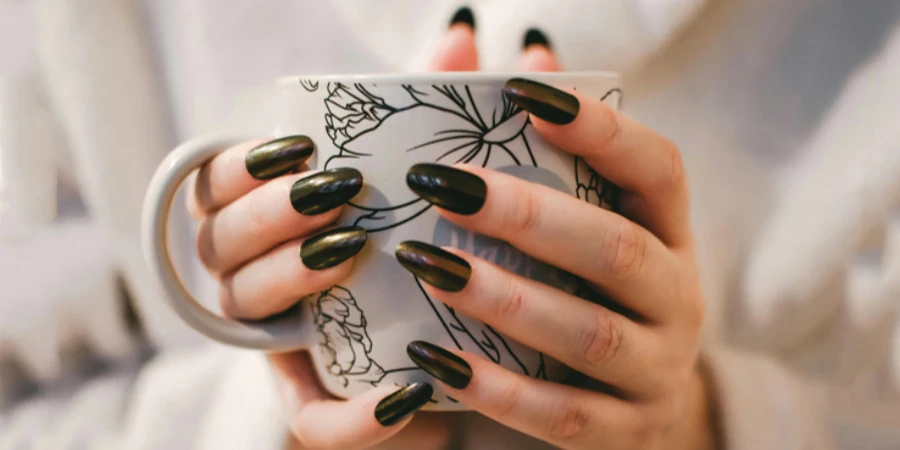 Woman With Black Manicure Holding White and Grey Floral Ceramic Cup