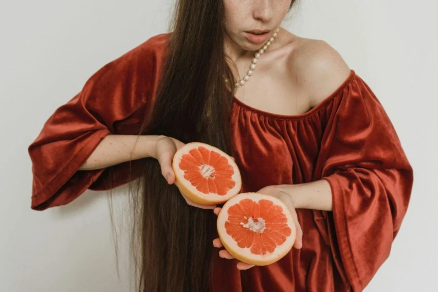 Woman in a red dress and pearl necklace holding a sliced grapefruit