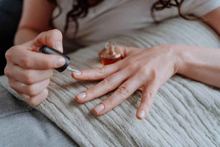 Woman painting clear gloss on nails on couch