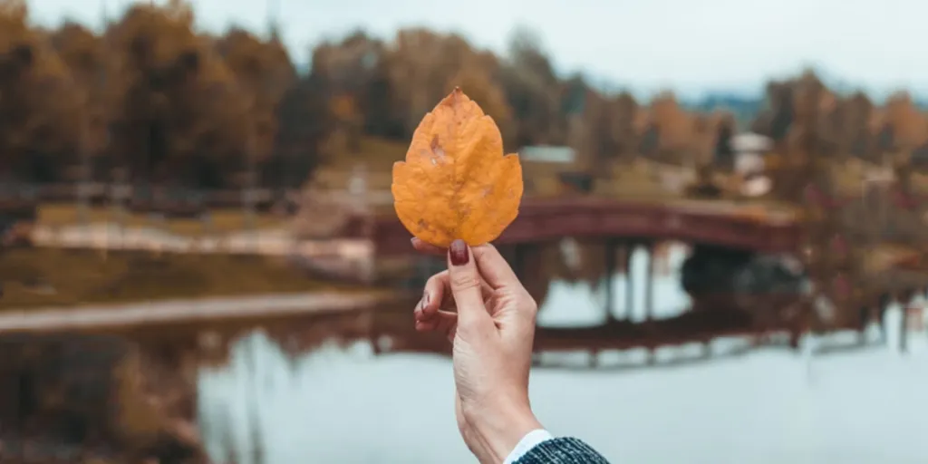 Woman with fall nails holding orange leaf at lake