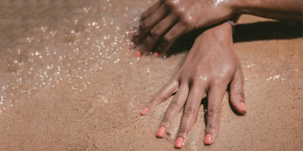 Woman’s hands in wet sand with nude summer nail designs