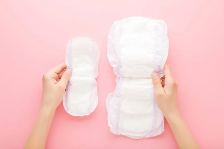 Young Adult Woman Hands Holding Opened White Sanitary Towels on Pink Table Background