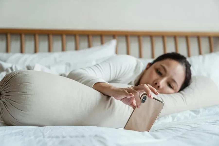 A woman lying in bed and using a smartphone