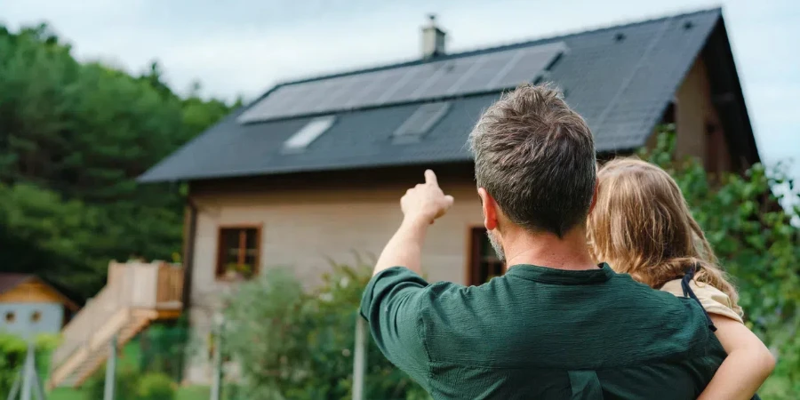 dad holding her little girl in arms and showing at their house with solar panels