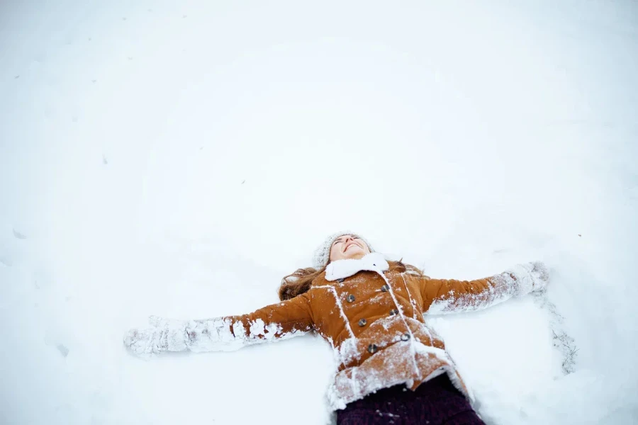 Woman in a peacoat lying on snow