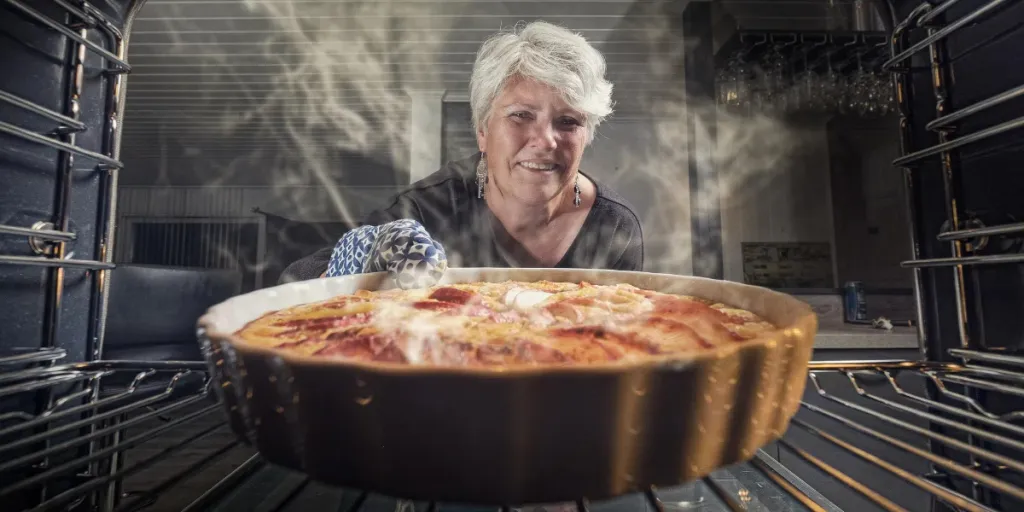 Woman taking out apple pie from an oven