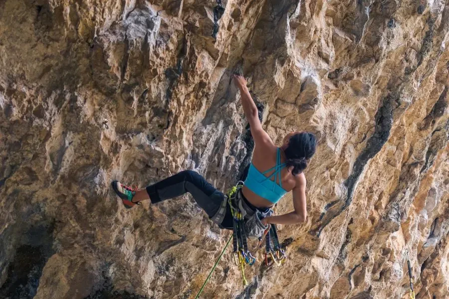 A woman is climbing a rock wall and wearing a blue top and black pants
