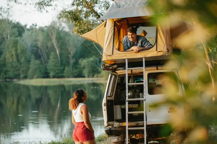 A couple enjoying a summer camping trip by a scenic lakeside in a rooftop tent