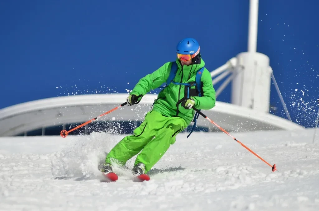 A skier in vibrant gear carves through fresh snow on a sunny winter day